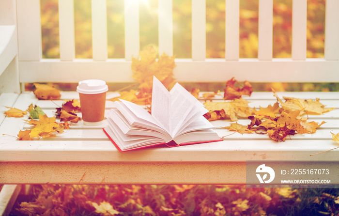 open book and coffee cup on bench in autumn park