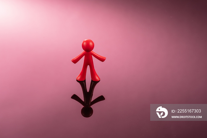 Red plastic figure of a man standing on a mirror pink surface