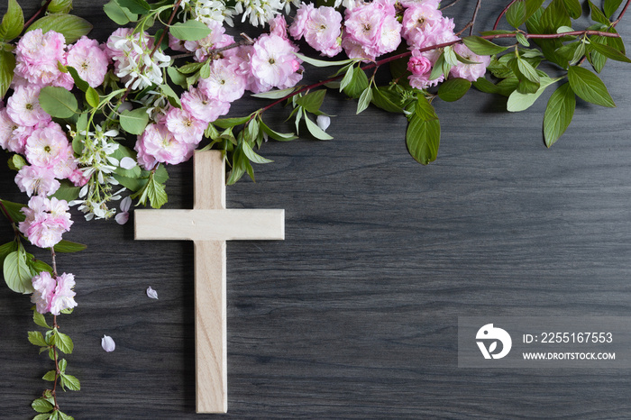 Wood cross with border of branches with pink and white flower blossoms on a dark wood background with copy space