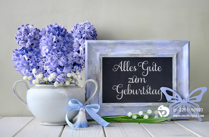 Blue decorations and hyacinth flowers on white table, blackboard with text  Alles gute zum geburtstag