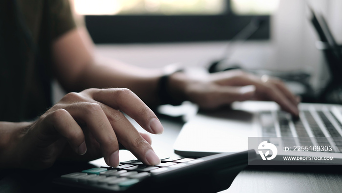 Close up Businessman using calculator and laptop for do math finance on wooden desk in office and business working background, tax, accounting, statistics and analytic research concept