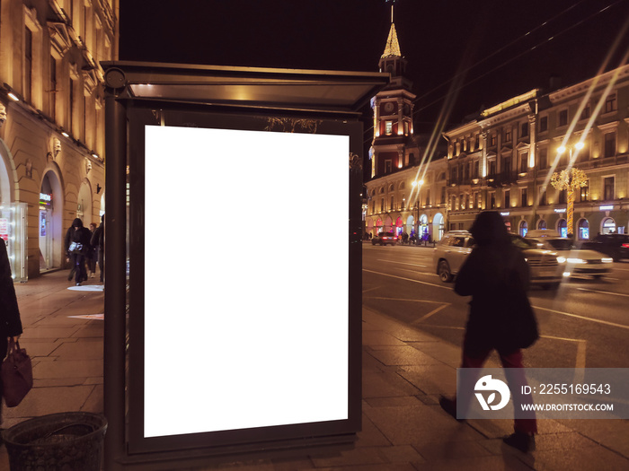 billboard in a bus stop. Glowing box with an advertising poster standing in the city at night. With people walking and riding cars