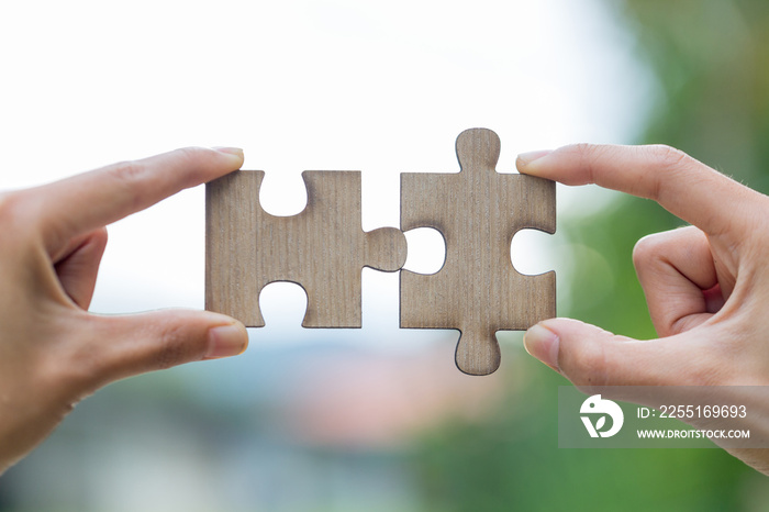 Two hands trying to connect couple puzzle piece with green background.  symbol of association and connection. business strategy.