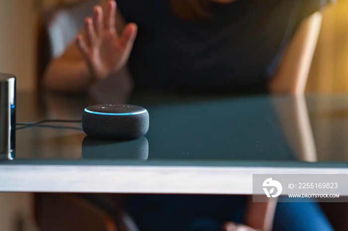 Woman sitting on a chair and talking to a speech recognition device, Amazon Alexa with sunlight background