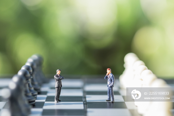 Business and work concept. Two businessmen miniature mini people figures standing and face to face on chessboard with black and white chess pieces