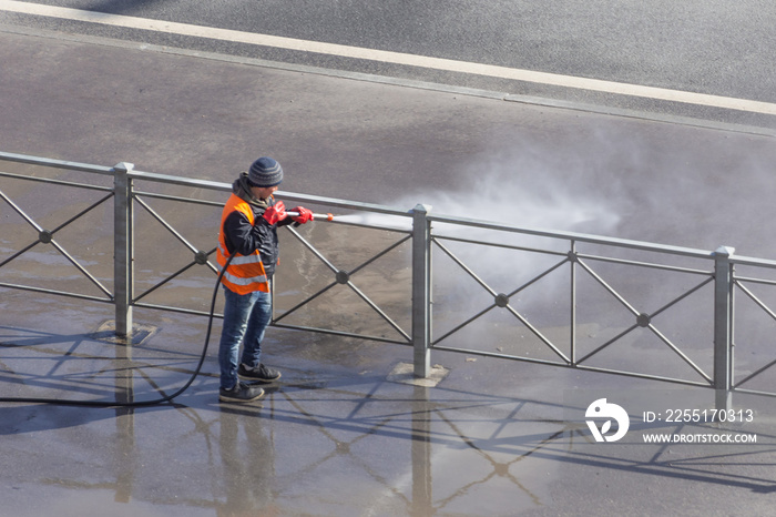 Worker cleaning driveway with gasoline high pressure washer splashing the dirt, asphalt road fence. High pressure cleaning.