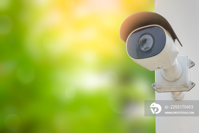 CCTV with water proof cover installed on wall in the blurred green tree background with orange sunlight. Digital security camera technology concept of surveillance monitoring for public safety.