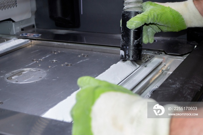 A male worker cleans the surface of an industrial 3D printer from white powder with a vacuum cleaner close-up. Multi Jet Fusion MJF 3D printing. The working process. 3d printing technology