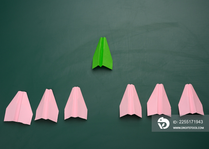 group of pink paper planes follow the first green airplane against a green background. The concept of uniting a team to achieve goals