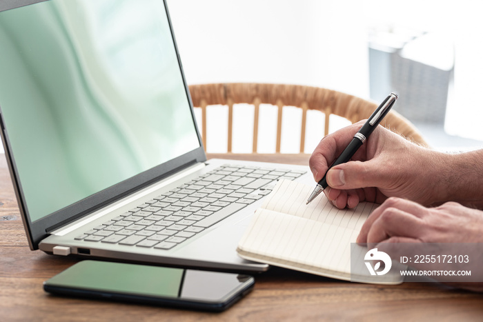 man taking notes on paper while using laptop computer, e-learning or working from home concept