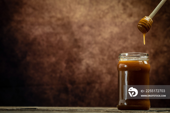 Sweet honey in glass jar and spoon on wooden background. Bees produce fresh, healthy, honey. Honey background. Beekeeping concept