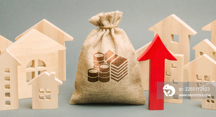 Red arrow up, money bag and miniature wooden houses. The concept of rising property prices. High mortgage rates. Expensive rental apartment. Growing demand for home purchase. Real estate market.