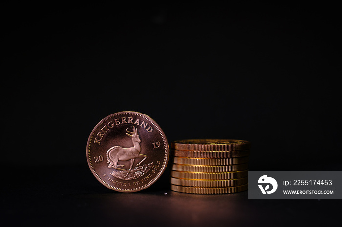 a Krugerrand gold coin stands next to a stack of gold coins on a dark background