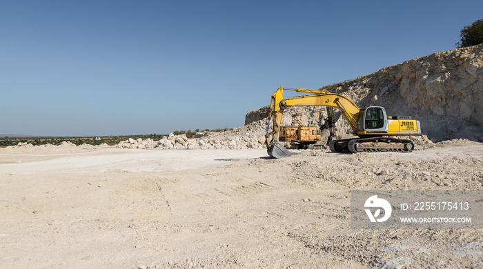 A large yellow tracked excavator is mining rock in a quarry.