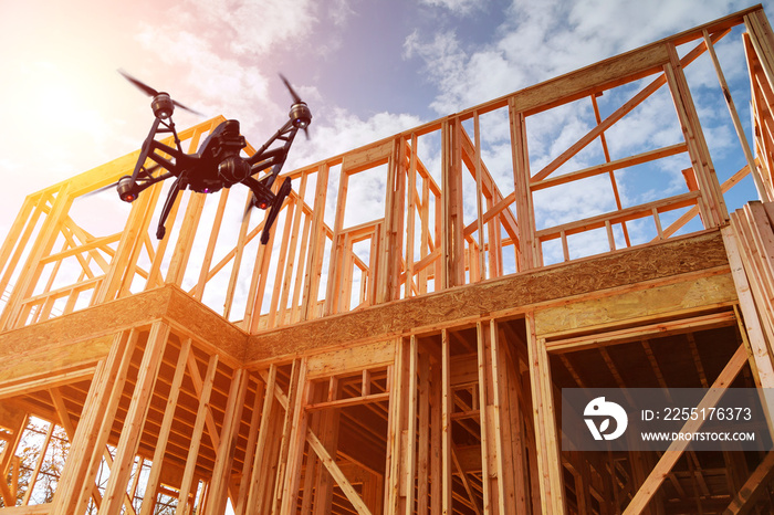 Black drone quadcopter with camera flying over residential construction home framing against a blue sky.