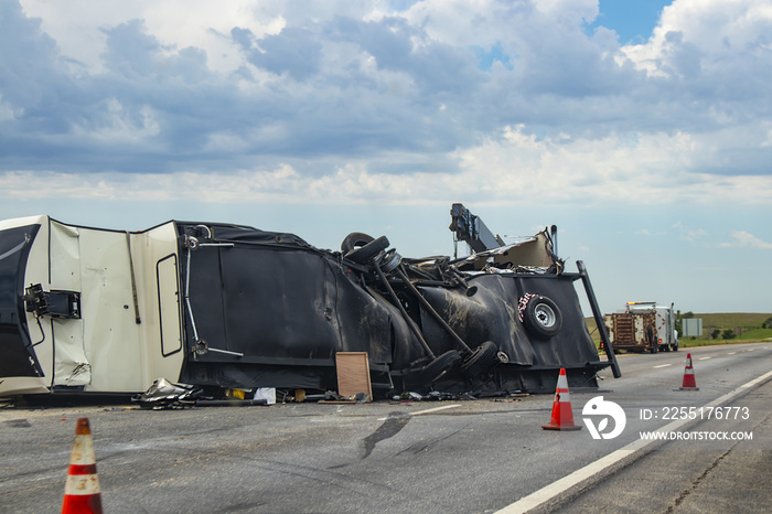 Fifth wheel Recreational Vehicle overturned on a highway with the underside torn up and things spilling out into the roadway after an accident