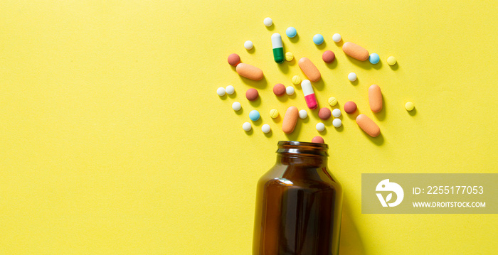 Pills and pill bottles on yellow background and text space,Banner with pills scattered from a bottle on a yellow surface. Place for an inscription.