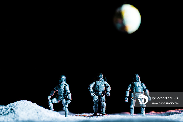 Toy soldiers standing on planet in space on black background with planet earth