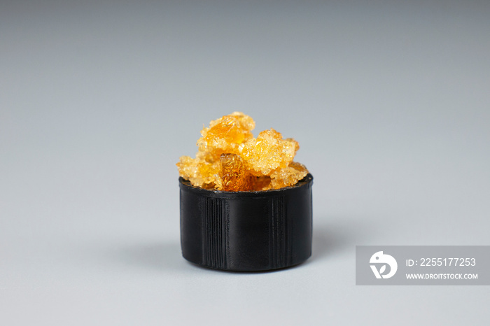 golden crystals of cannabis wax, glass container with crumbs of marijuana concentrate and copy space