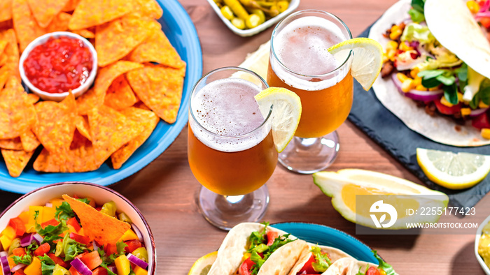 Table with tacos, mango salsa, nachos with sauce, guacamole, lemon beer. Appetizers and traditional mexican dishes for cinco de mayo or taco tuesday on wooden table top, copy space