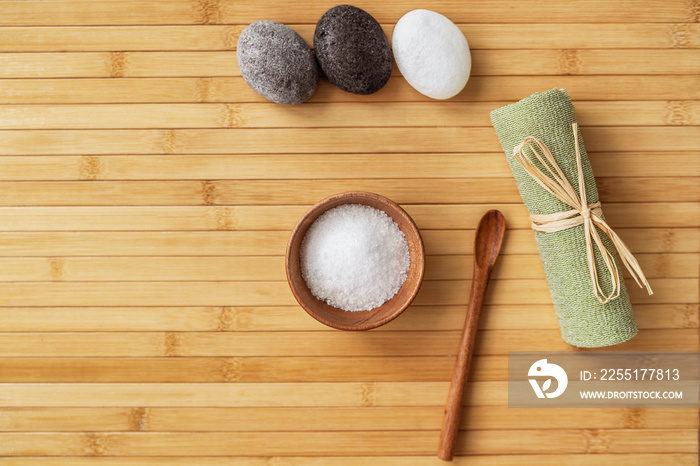 Bath salts natural spa products top view on bamboo wooden texture background with copy space for wellness health concepts. Hot stone massage and exfoliation towel salt in wood bowl.