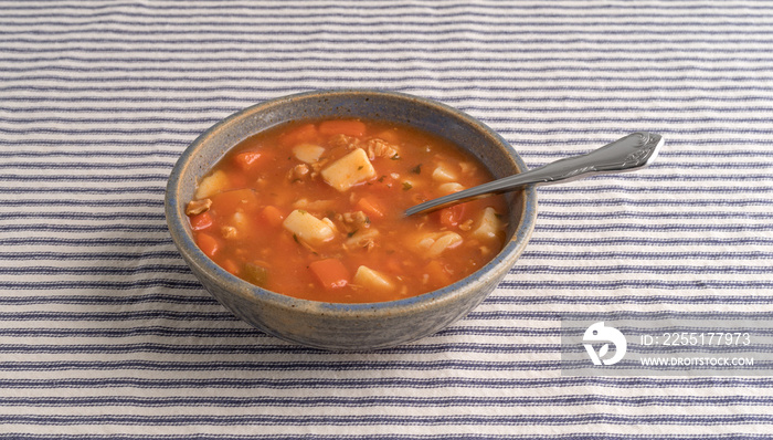 Bowl of Manhattan style clam chowder with spoon on a striped tablecloth.