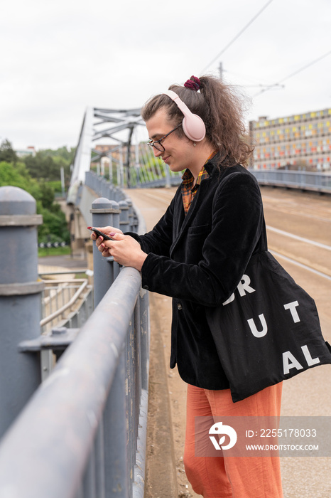 Young man listening music on phone while leaning on railing on city street