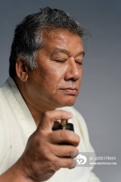 Portrait of serious man putting on perfume against gray background