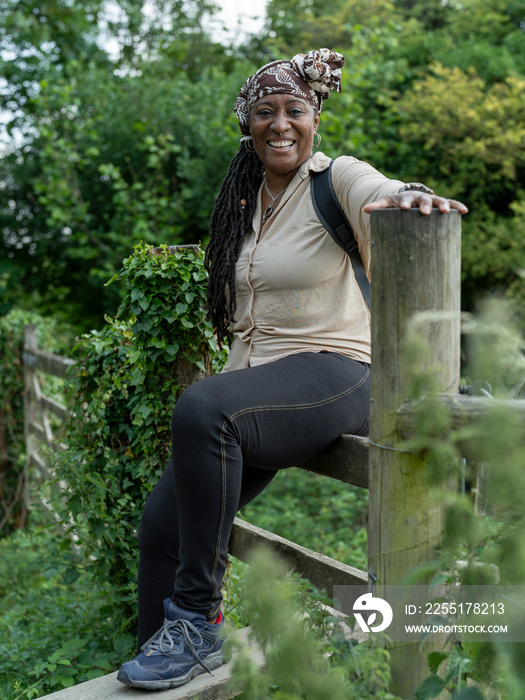 Portrait of smiling mature woman sitting on fence on hike