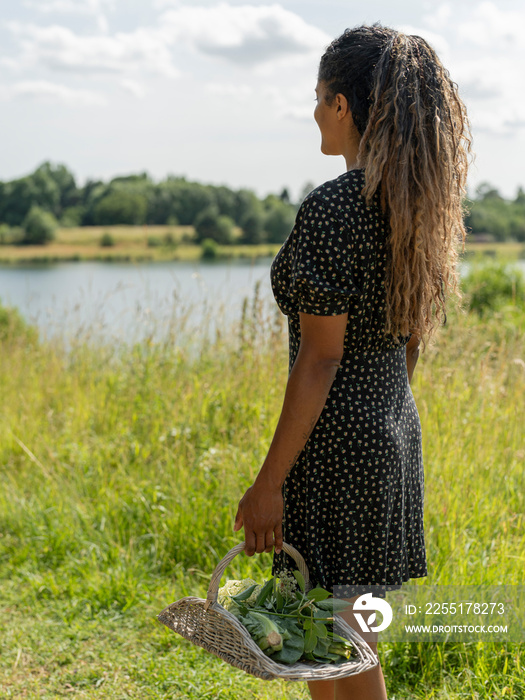 Woman with basket looking at lake on sunny day