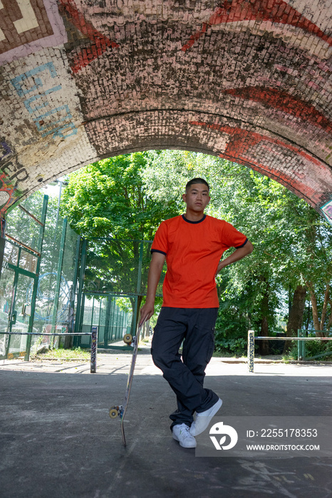 Portrait of young male skateboarder standing under brick arch