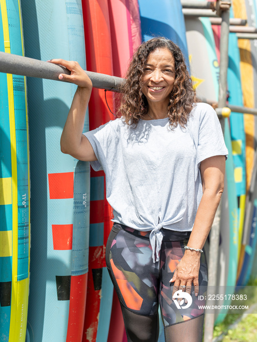 Portrait of smiling woman standing next to paddleboard rack