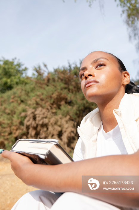 Portrait of pensive woman with book on beach