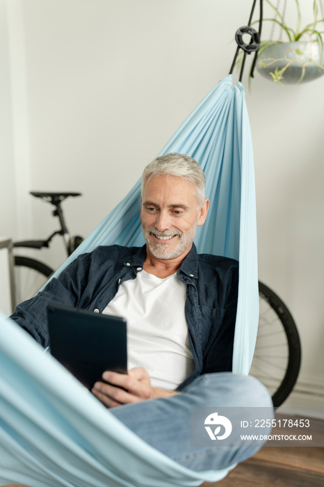 Smiling mature man using digital tablet in hammock