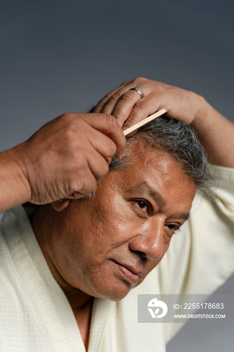 Portrait of serious man combing hair against gray background