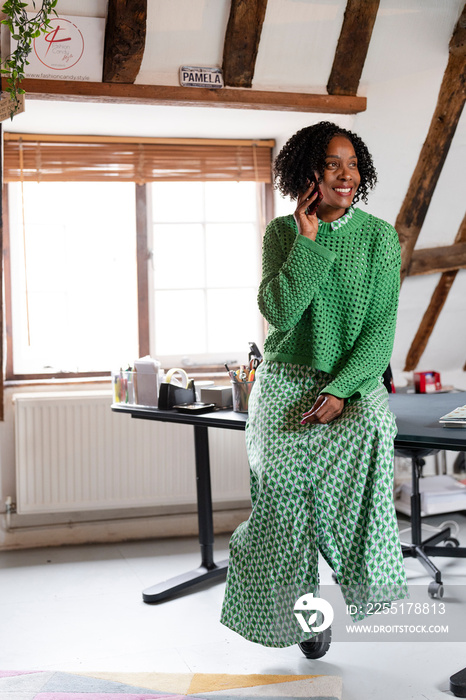 Businesswoman talking by phone while sitting on desk in office