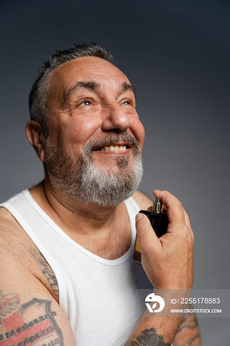 Portrait of senior man putting on perfume against gray background