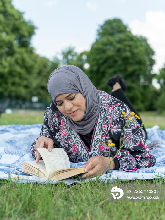 UK,Sutton,Woman in headscarf reading book on lawn in park