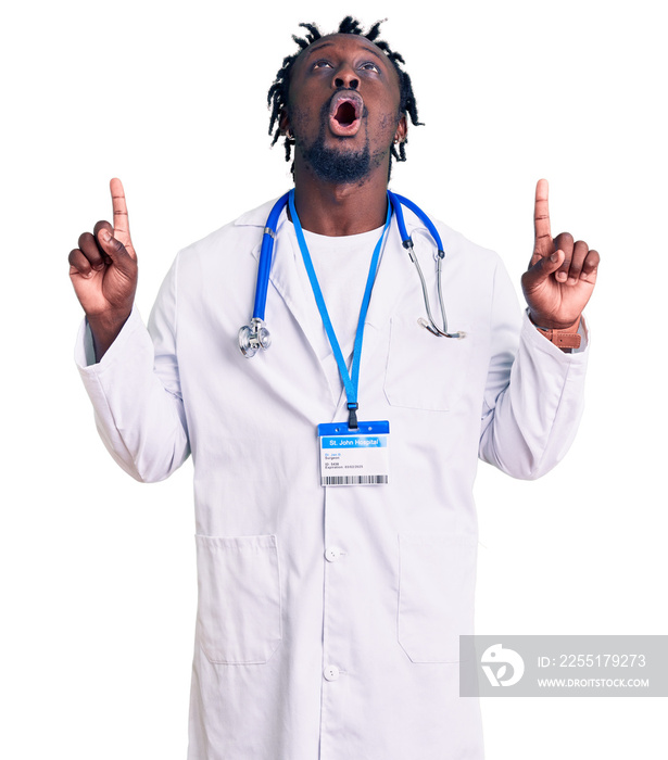 Young african american man with braids wearing doctor stethoscope and id pass amazed and surprised looking up and pointing with fingers and raised arms.