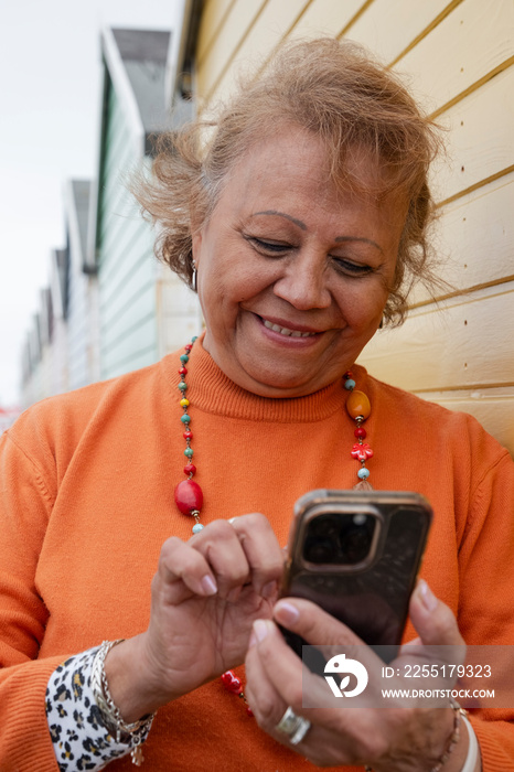 Smiling senior woman using smart phone by beach hut