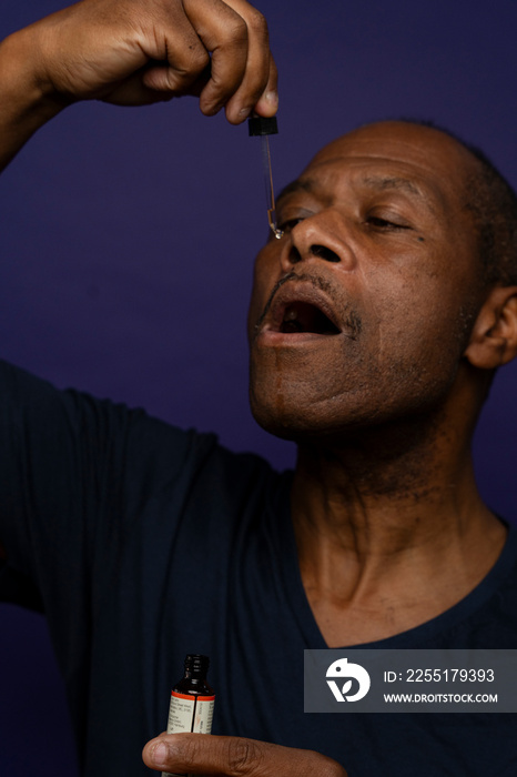 Man taking medicine with pipette against purple background