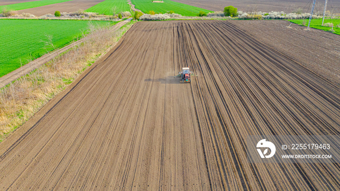 Aerial view of tractor as dragging a sowing machine over agricultural field, farmland