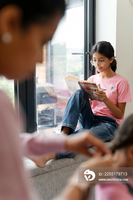 Girl sitting at hassock near window and reading book