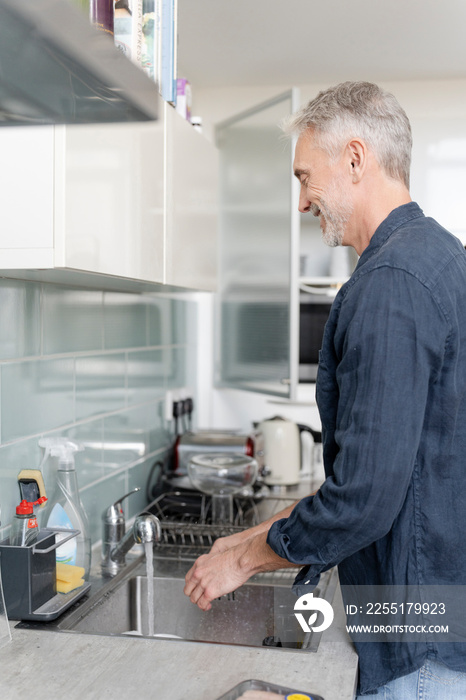 Mature man washing hands in kitchen sink