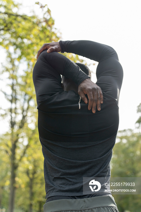 Rear view of athletic man stretching arm in park