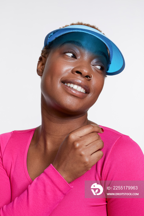 Studio portrait of smiling woman wearing blue sun visor and pink shirt