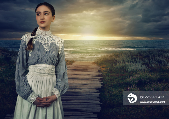 Young victorian girl in white dress and blue striped blouse on the coast at sunset.