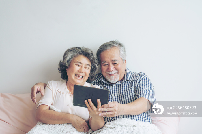 Senior couple using a tablet phone computer face time call to relatives descendant relatives grandchild, smiling feel happy in sofa at home - lifestyle senior concept