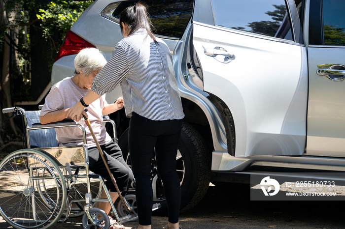 Asian female caregiver helping disabled elderly woman in wheelchair to get into the car,helpful daughter care and support senior mother to stand up from wheelchair in outdoor, caring for old people