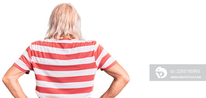 Old senior man with grey hair and long beard wearing striped tshirt standing backwards looking away with arms on body